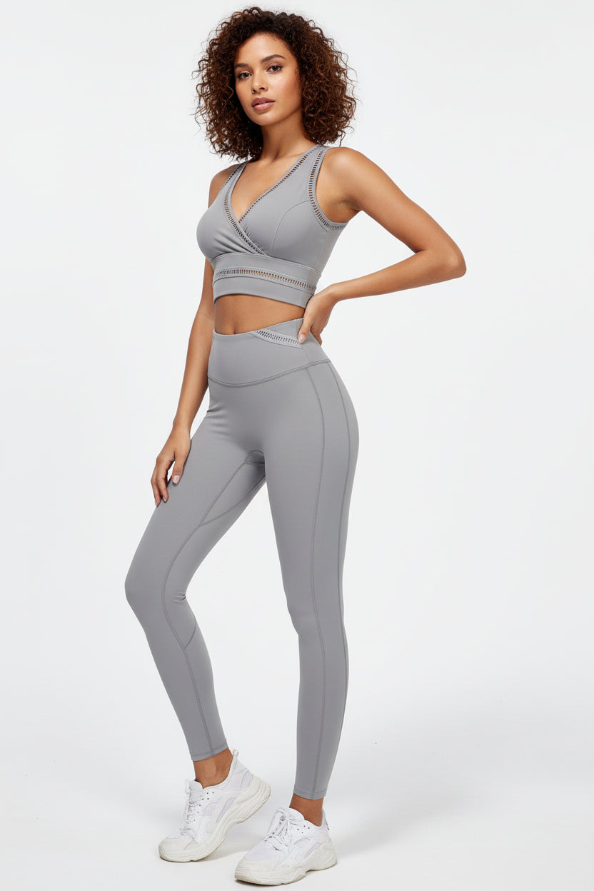 A female model wearing a white outfit consisting of a sports bra and leggings, holding a pink exercise ball, against a white background.