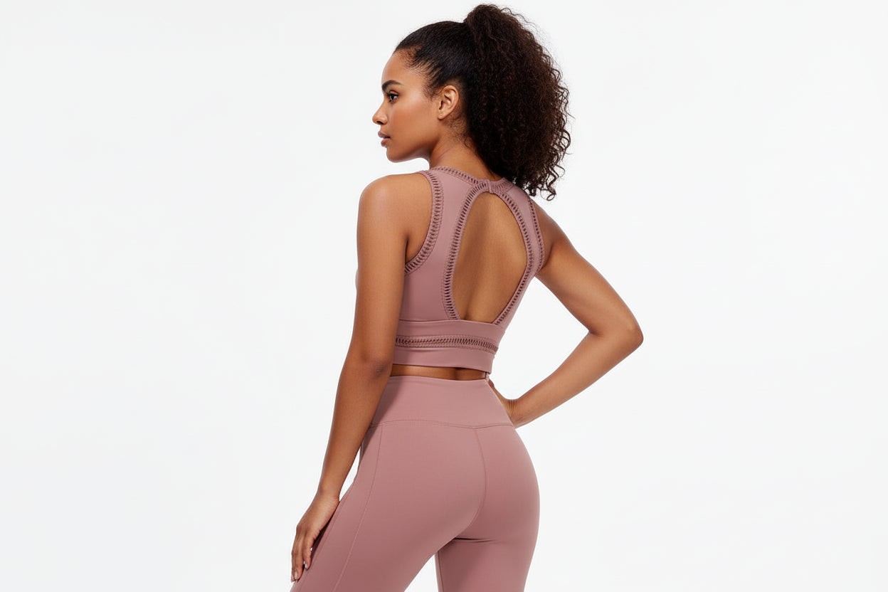 A female model wearing a white outfit consisting of a sports bra and leggings, holding a pink exercise ball, against a white background.