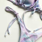 Pastel tie-dye bikini set on a wooden surface with green leaves.