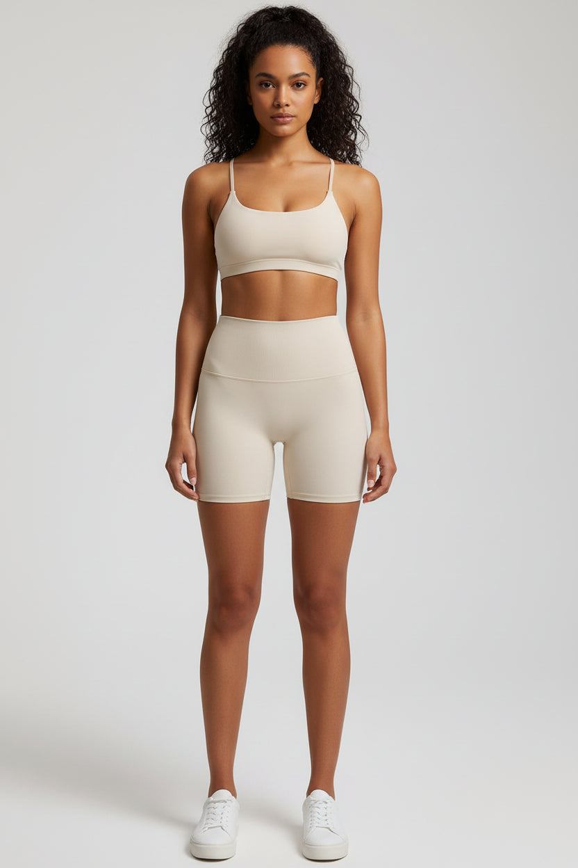 A woman standing wearing a beige tank top and matching leggings, against a white background.